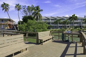Una terraza de madera con bancos, una piscina y un edificio con balcones al fondo.