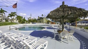 A swimming pool with lounge chairs and a thatched umbrella, surrounded by palm trees and a clear sky. - Sunset Cove: One-Bedroom in Treasure Island (Treasure Island)