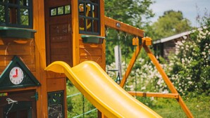 A wooden playhouse with a yellow slide and a clock. - Anchorage House & Cottages - Anchorage House (Hubbards)