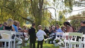 A wedding ceremony outdoors with guests seated on white chairs arranged in rows. - Anchorage House & Cottages - Anchorage House (Hubbards)