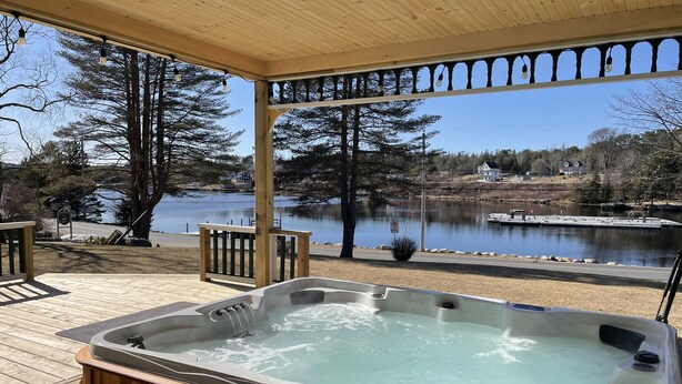 A hot tub on a wooden deck with a view of a lake and trees. - Anchorage House & Cottages - Anchorage House (Hubbards)