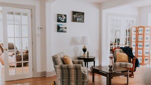 A living room with a striped armchair, a small table with a lamp, and a bookshelf filled with books. - Anchorage House & Cottages - Anchorage House (Hubbards)