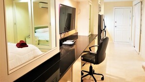Ein Hotelzimmer mit einem Bett, einem Schreibtisch mit Computer, einem Sessel, einem Fernseher und einem Kleiderschrank.