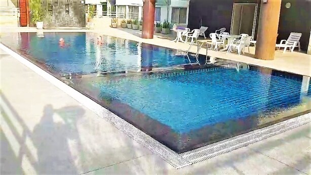Ein rechteckiger, überdachter Swimmingpool mit klarem, blauem Wasser, umgeben von Liegestühlen und Topfpflanzen.