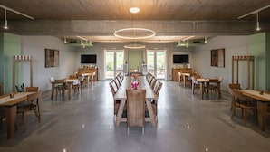 A spacious dining area with a long wooden table and chairs, a modern circular light fixture, and large windows offering a view of greenery outside. - Il Cru di Vignanova (Castagneto Carducci)