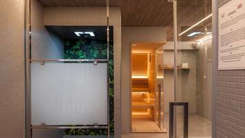 Un interno moderno con una porta in vetro che dà sull'area sauna, una parete rivestita di piastrelle con motivo a griglia e una panca in legno.