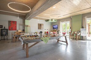 A spacious room with a long table set for a buffet, wooden beams on the ceiling, a television, and artwork on the walls. - Il Cru di Vignanova (Castagneto Carducci)