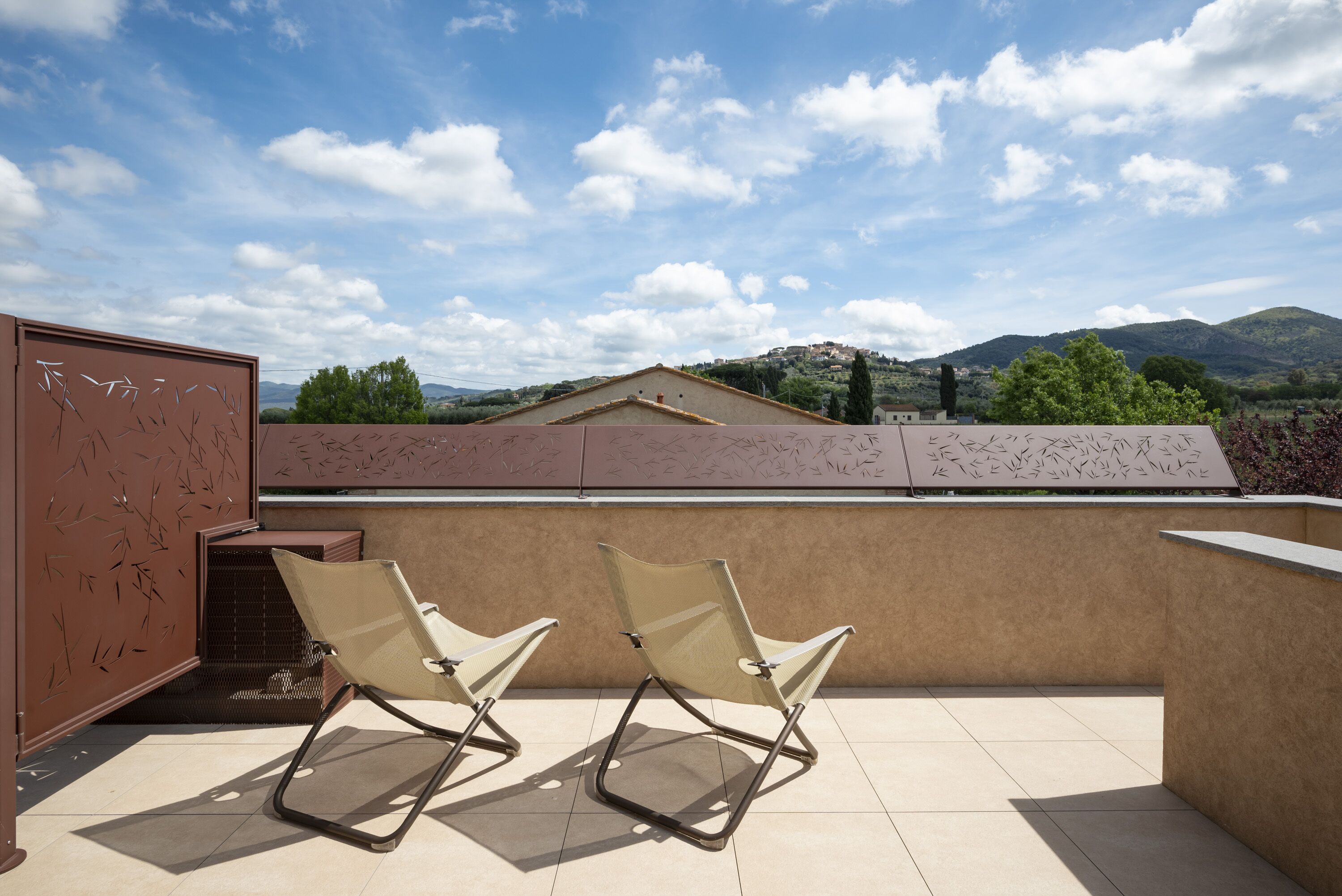 A rooftop terrace with two beige chairs and a view of a mountainous landscape.
