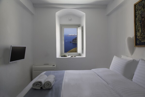 Une chambre à coucher avec un lit, une fenêtre donnant sur la mer, un téléviseur à écran plat et une table de chevet.