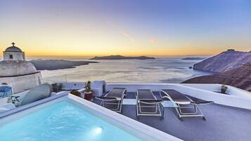 Una piscina infinita en la azotea con sillones y vistas al mar al atardecer.