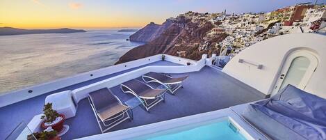 A pool area with lounge chairs and a view of the sea and coastal buildings.