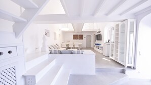 Un interior moderno y blanco con una escalera que lleva a una sala de estar, un comedor y una cocina.
