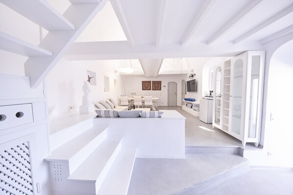 A modern, white interior with a staircase leading to a living area, a dining area, and a kitchen.