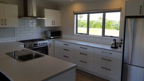 Een moderne keuken met witte kasten, een roestvrijstalen koelkast, een magnetron, een fornuis en een raam met uitzicht op groen.