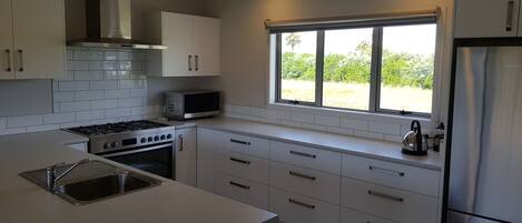A modern kitchen with white cabinets, a stainless steel refrigerator, a microwave, a stove, and a window with a view of greenery.
