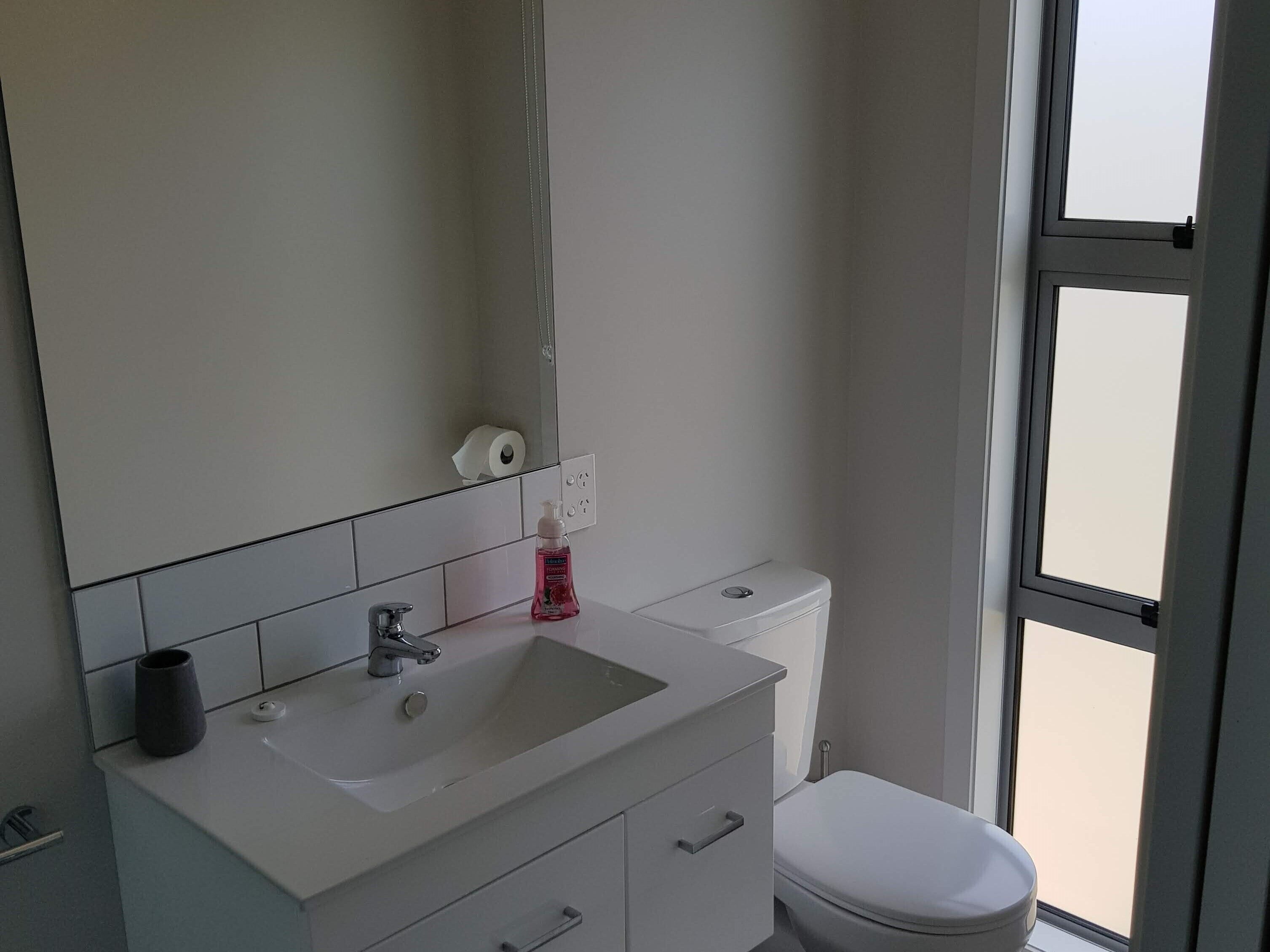 Un baño con lavamanos, espejo y inodoro blancos.