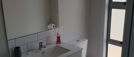 Un baño con lavamanos, espejo y inodoro blancos.
