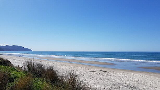 Een strand met heldere lucht, een zandstrand en een bergketen in de verte.