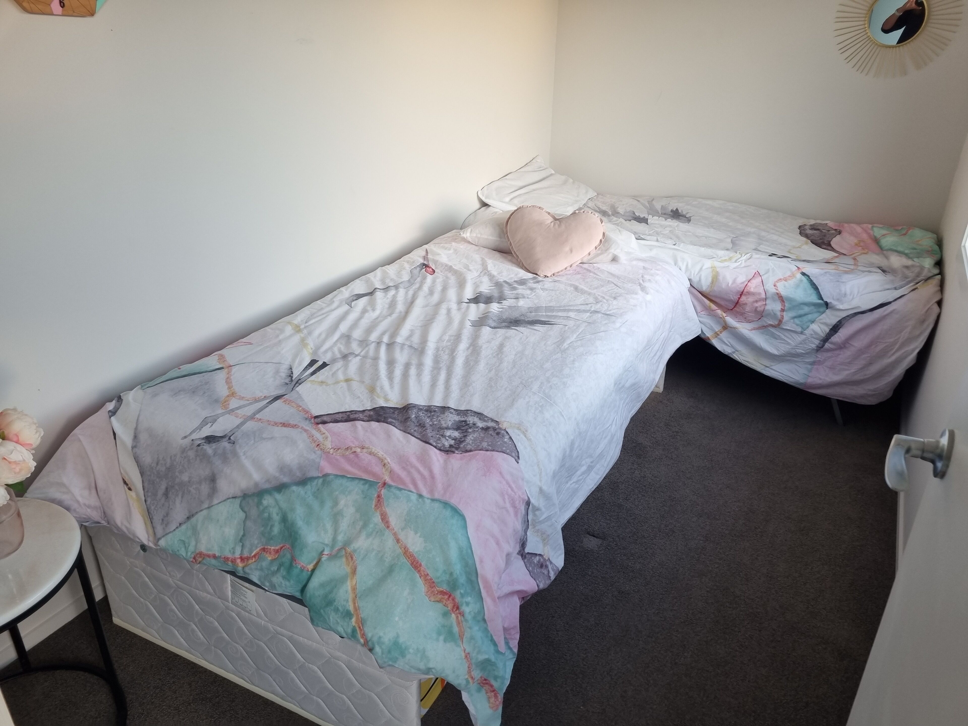 Una habitación pequeña con una cama individual, un edredón colorido, una mesita de noche y un espejo en la pared.