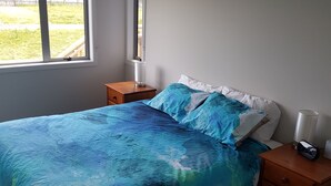 Een slaapkamer met een bed, nachtkastjes, een lamp en een raam met uitzicht op het omliggende landschap.