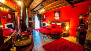 Une chambre dotée d’un grand lit, de murs en pierre et d’une décoration aux tons rouges.