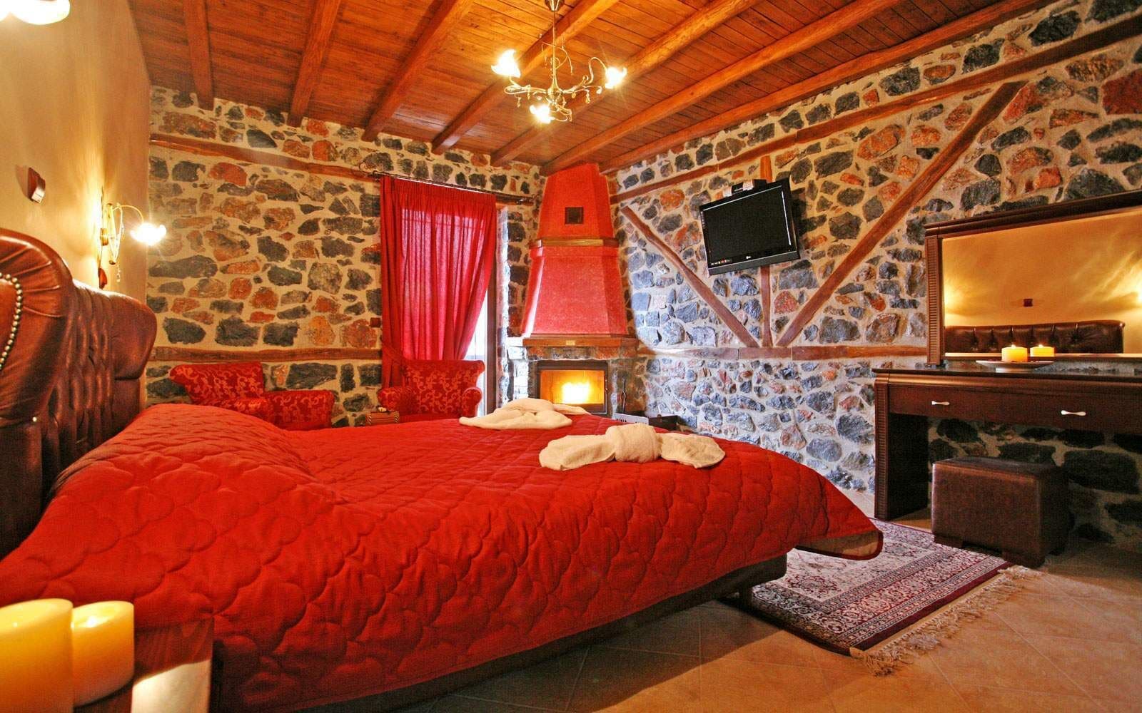 A cozy room with a large bed, stone walls, a fireplace, and a television.