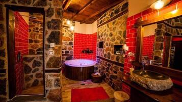 A stone-walled bathroom with a red-tiled shower area, a wooden bathtub, and a stone sink.