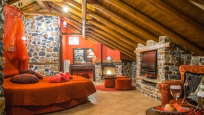 Une chambre confortable située dans les combles, avec un mur en pierre, une cheminée, une télévision et un lit avec une literie rouge.