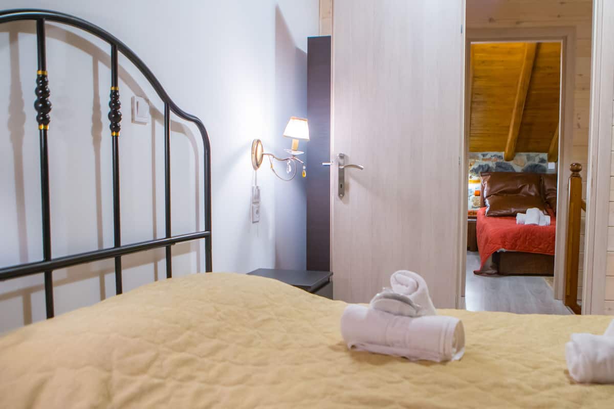A bedroom with a bed, a bedside table, a lamp, and a door leading to another room.
