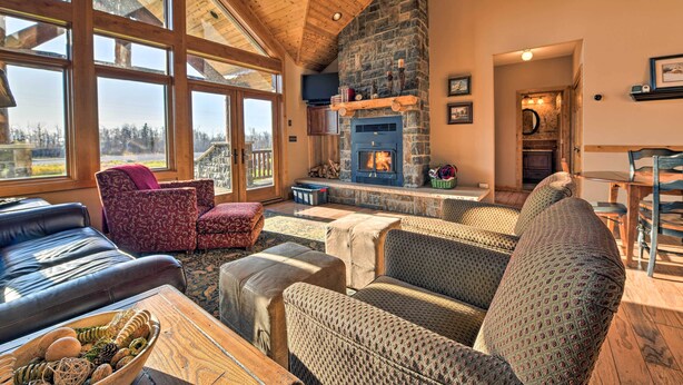 A cozy living room with a stone fireplace, large windows, and comfortable seating. - North Shore Cabin w/ Fire Pit By Gooseberry Falls! (Two Harbors)