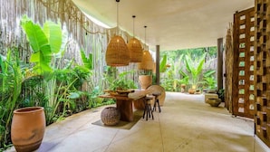 A tropical-style dining area with a wooden table, wicker hanging lights, and lush greenery. - Aldea Zama Condo w/ Private Rooftop Infinity Pool (Tulum)