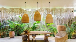 A dining area with a wooden table, two stools, and a woven chair. - Aldea Zama Condo w/ Private Rooftop Infinity Pool (Tulum)