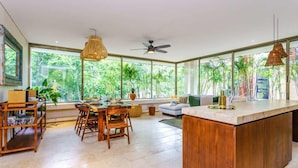 A spacious kitchen with a large island, wooden furniture, and large windows offering a view of lush greenery. - Aldea Zama Condo w/ Private Rooftop Infinity Pool (Tulum)