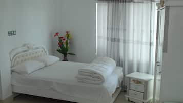 A neatly made bed with white linens, a bedside table with a drawer, and a vase with flowers.