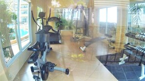 A gym with exercise equipment, a large window, and a view of a pool and buildings.