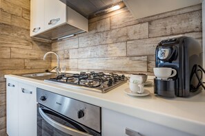 Une cuisine de taille réduite équipée d’une cuisinière à gaz, d’une machine à café et d’un évier.