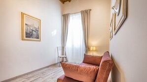 A room with a wooden floor, a cushioned seating area, a chair, a lamp, and a framed picture on the wall.