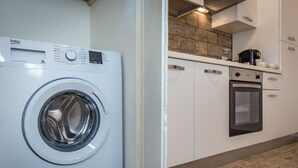 A modern kitchen with a built-in washing machine, a stove, and wooden flooring.