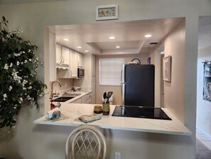A compact kitchen with white cabinets, a black refrigerator, and a built-in stove. - 402 - Fourth floor ocean view delight (New Smyrna Beach)