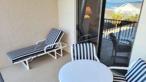 A balcony with two striped lounge chairs and a round table. - 402 - Fourth floor ocean view delight (New Smyrna Beach)