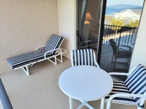 A balcony with two striped lounge chairs and a round table. - 402 - Fourth floor ocean view delight (New Smyrna Beach)
