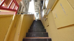 Eine enge Treppe mit roter Handläufung, die zu einer Tür oben führt.