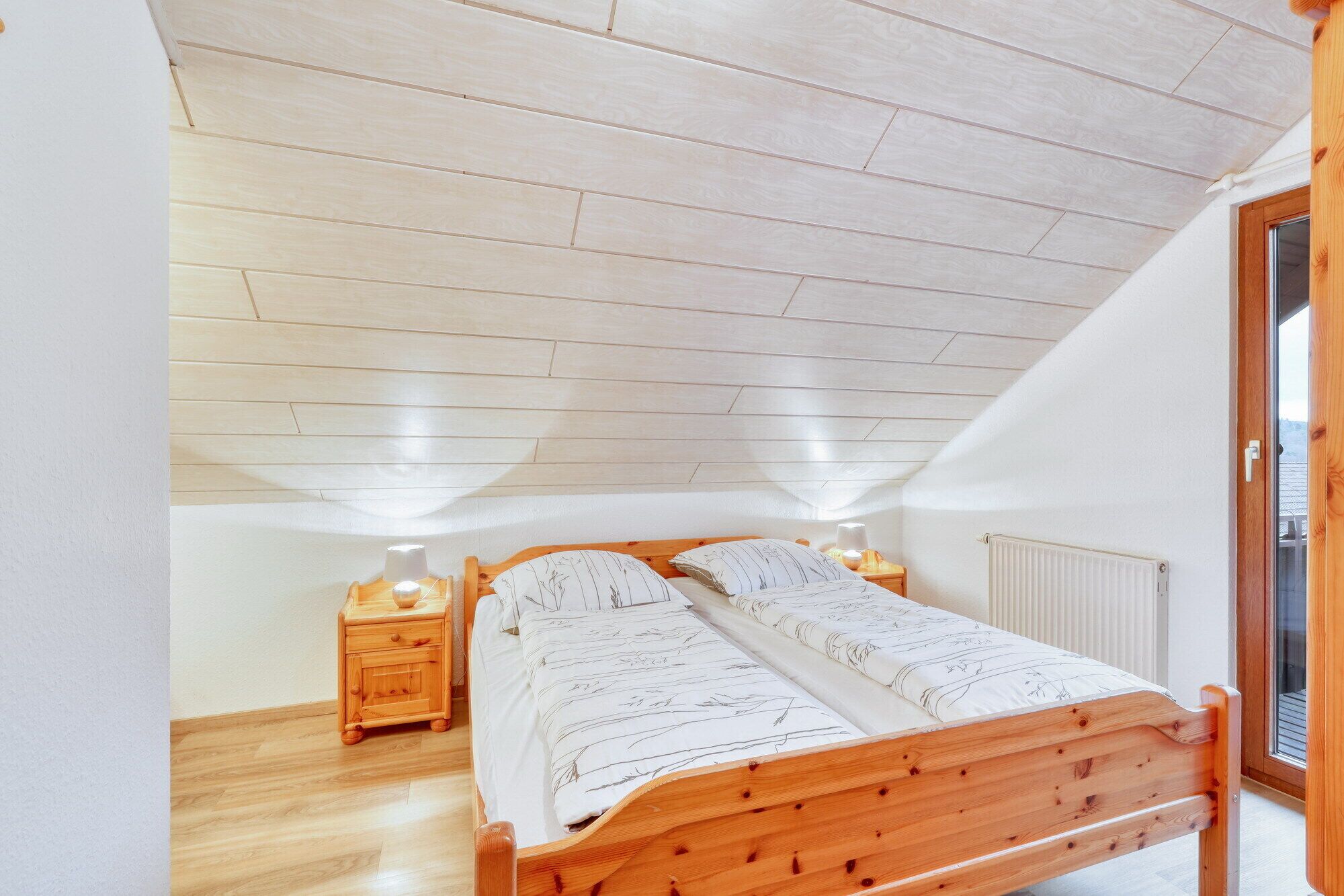 A bedroom with a sloped ceiling, wooden bed frame, two bedside tables, and a radiator.