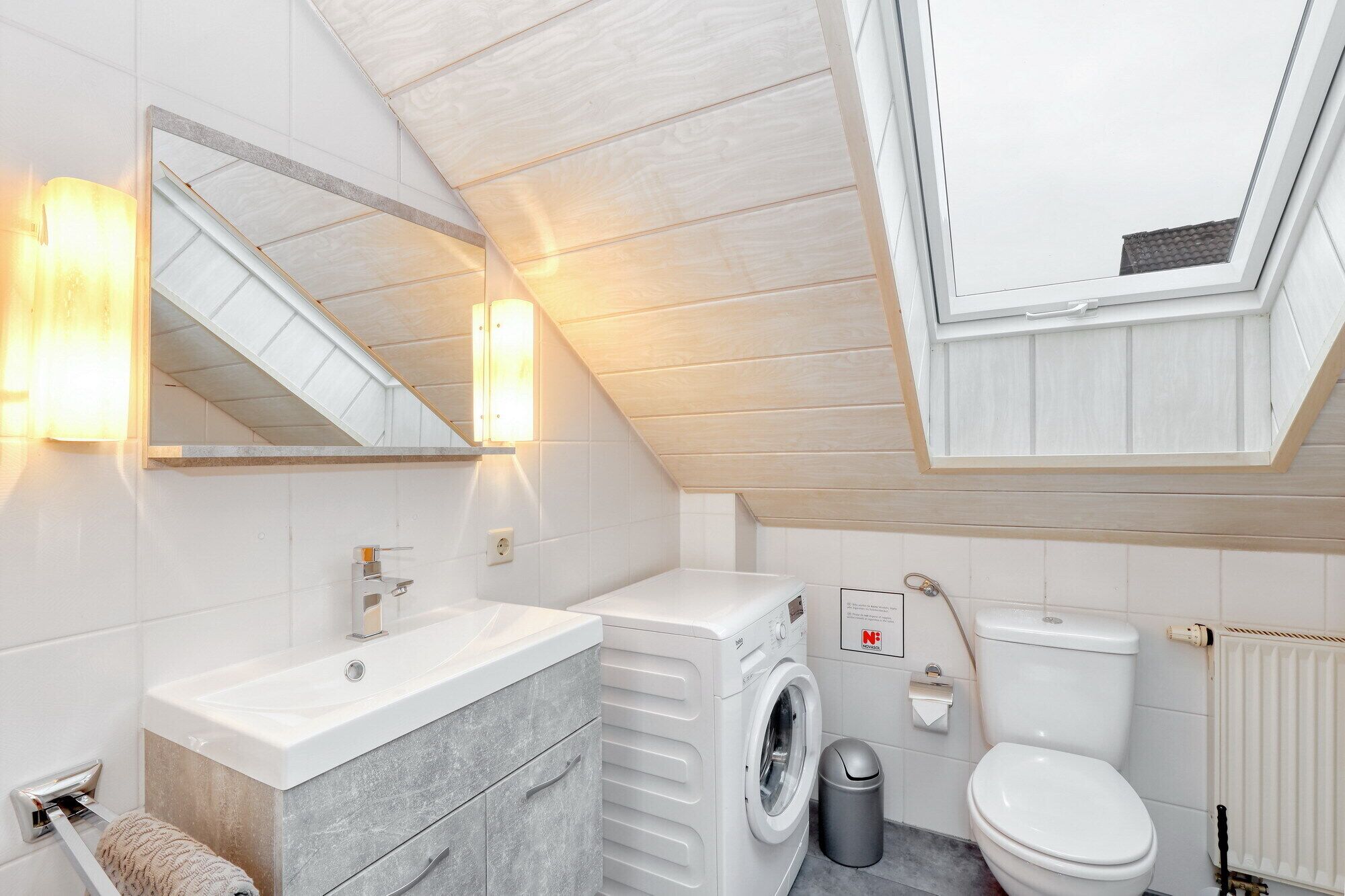 A modern bathroom with a skylight, a washing machine, a toilet, and a sink.