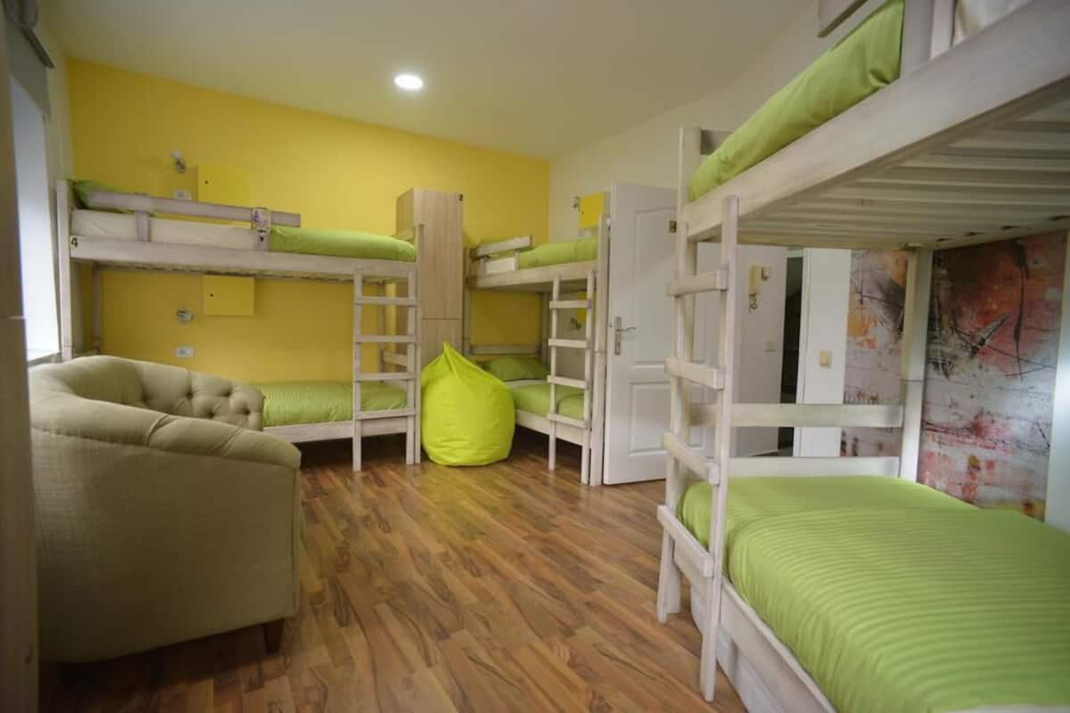 A dormitory room with bunk beds, a green bean bag chair, and a sofa.