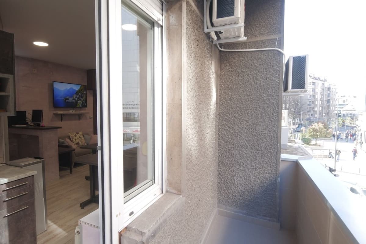 A balcony with a view of a cityscape, a kitchen area with a TV, and a sliding door leading to a living room.
