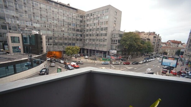 A balcony with a view of a busy street, buildings, and a few parked cars. - Hostel Stella Di Notte (Belgrade)