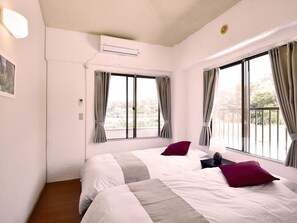A hotel room with two beds, a window with curtains, an air conditioning unit, and a small bedside table. - Bay Side Okinawa (Onna)