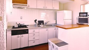 A compact kitchen with white cabinets, a built-in microwave, and a dishwasher. - Bay Side Okinawa (Onna)