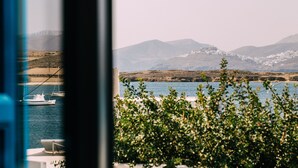 Udsigt over et kystlandskab med fortøjede både, et bjergkæde og en bygning med hvide vægge i baggrunden.